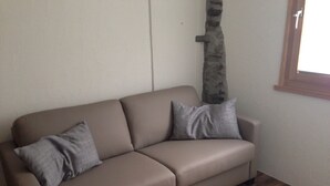 A beige sofa with two pillows against a plain wall and a wooden floor. - Rustico with style, modern and rustic, 2-4 P, in Val Poschiavo (Poschiavo)