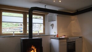 A compact kitchen with a wood-burning stove, a small oven, and a window with a view of greenery outside. - Rustico with style, modern and rustic, 2-4 P, in Val Poschiavo (Poschiavo)