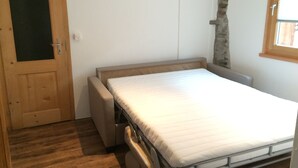 A small, single-bed room with a wooden door, a stone wall, and a window. - Rustico with style, modern and rustic, 2-4 P, in Val Poschiavo (Poschiavo)
