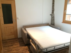 A small, single-bed room with a wooden door, a stone wall, and a window. - Rustico with style, modern and rustic, 2-4 P, in Val Poschiavo (Poschiavo)