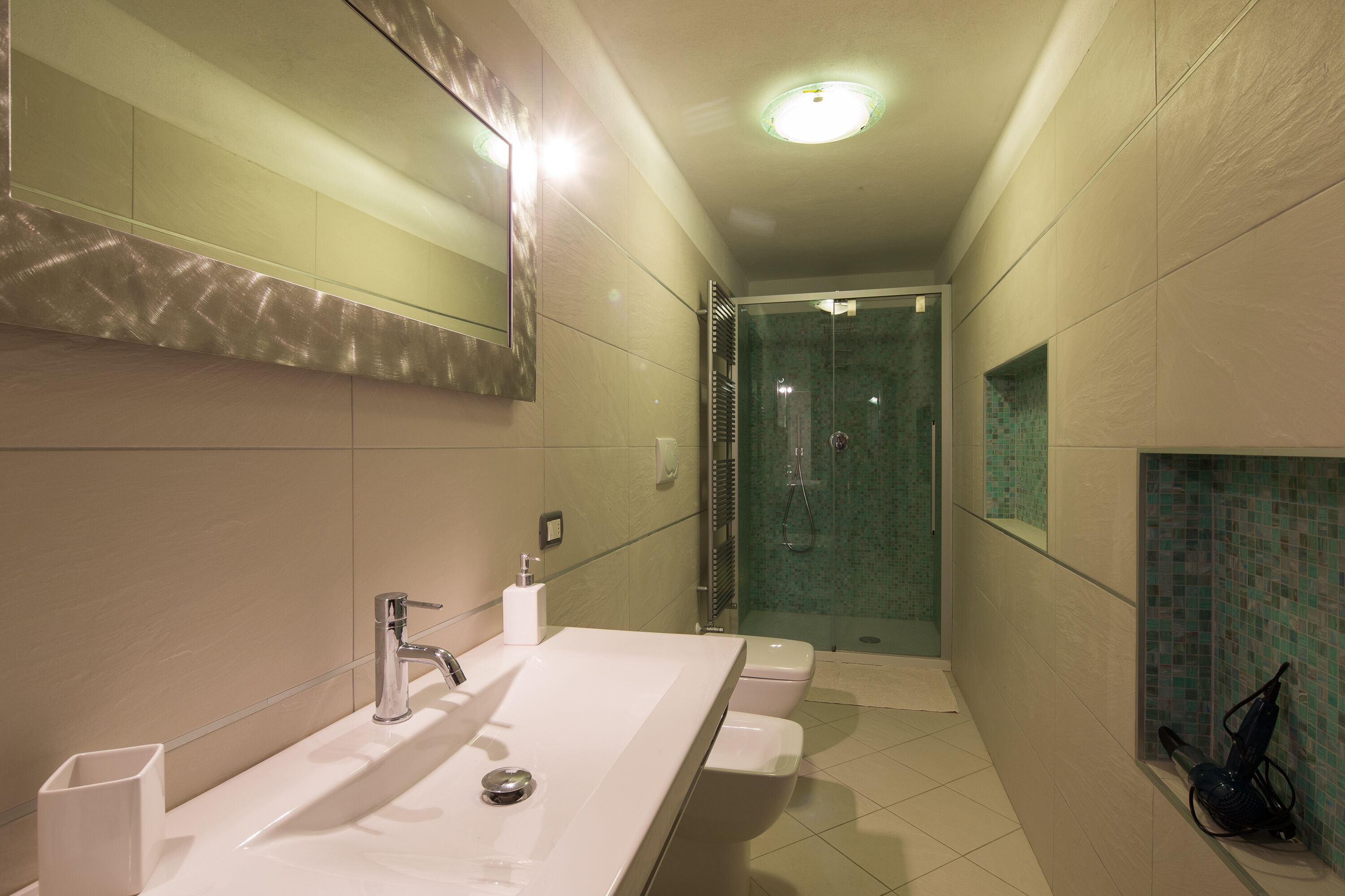 A modern bathroom with a large mirror, a sink, and a shower area.