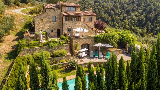 Une villa en pierre dotée d’une piscine, entourée d’une végétation luxuriante et de collines.