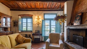 Un salon chaleureux avec un plafond en bois, un canapé, un fauteuil, une cheminée et une vue par les fenêtres.
