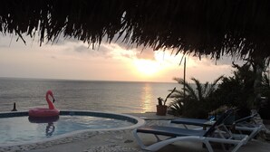 Una piscina con un flotador de flamenco, sillas de descanso y vistas al atardecer.