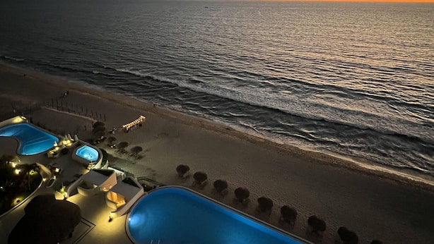 Un complexe hôtelier en bord de mer doté d’une piscine, de chaises longues et offrant une vue sur le coucher de soleil.
