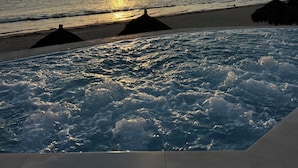 Une vue sur la plage avec un coucher de soleil, des vagues de l’océan et des parasols en chaume.