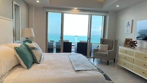 Une chambre à coucher avec un lit, un ventilateur de plafond, une commode et une vue sur l’océan grâce à de grandes fenêtres.