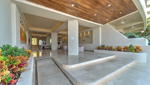 Un hall d’entrée moderne avec un plafond en bois, un escalier central et un espace détente offrant une vue sur l’intérieur.