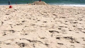 En sandstrand med fodspor og et par personer i det fjerne.
