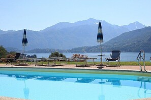 Ein Pool mit Liegestühlen und Sonnenschirmen mit Blick auf einen See und Berge.