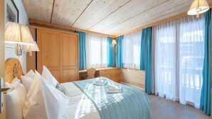 Habitación de hotel con techo de madera, cama con ropa blanca, escritorio y ventana con cortinas azules.