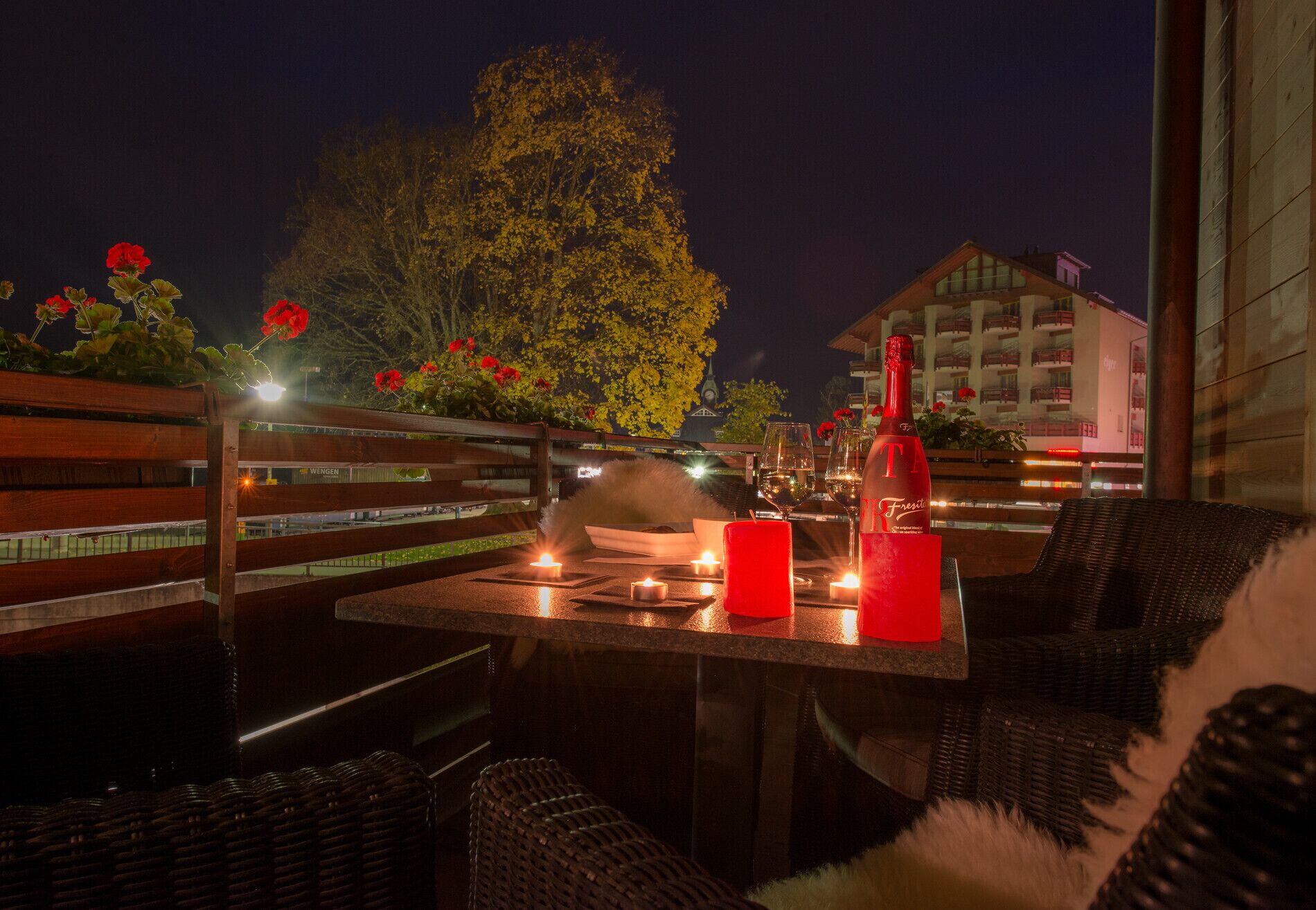 An outdoor dining area with wicker furniture, candles, and a bottle of red wine.