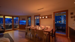 Ein Essbereich mit Holztisch für vier Personen, großen Fenstern mit Blick auf die Stadtlandschaft und einer darüber hängenden Chandelier.