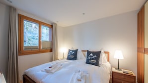 Ein ordentlich bezogenes Bett mit Kissen, ein Nachttisch mit Lampe und ein Fenster mit Vorhängen.