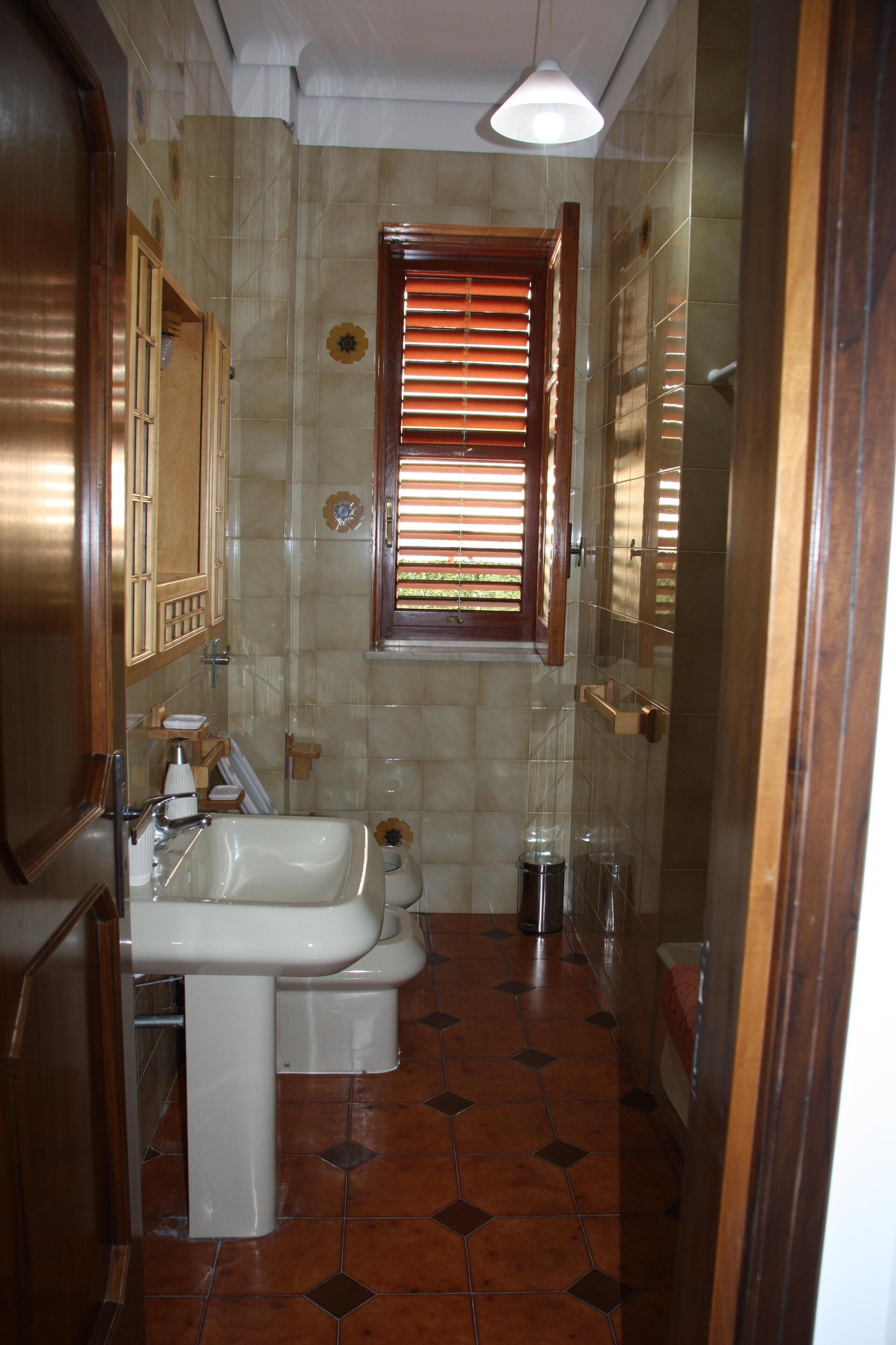 Une salle de bain avec un lavabo, un miroir et une fenêtre équipée de stores.