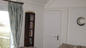 Een woonkamer met een beige fauteuil, een bank, een boekenkast en een deur met een maanverloting.