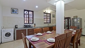 A dining area with a wooden table set for four, a washing machine, and a refrigerator in the background.