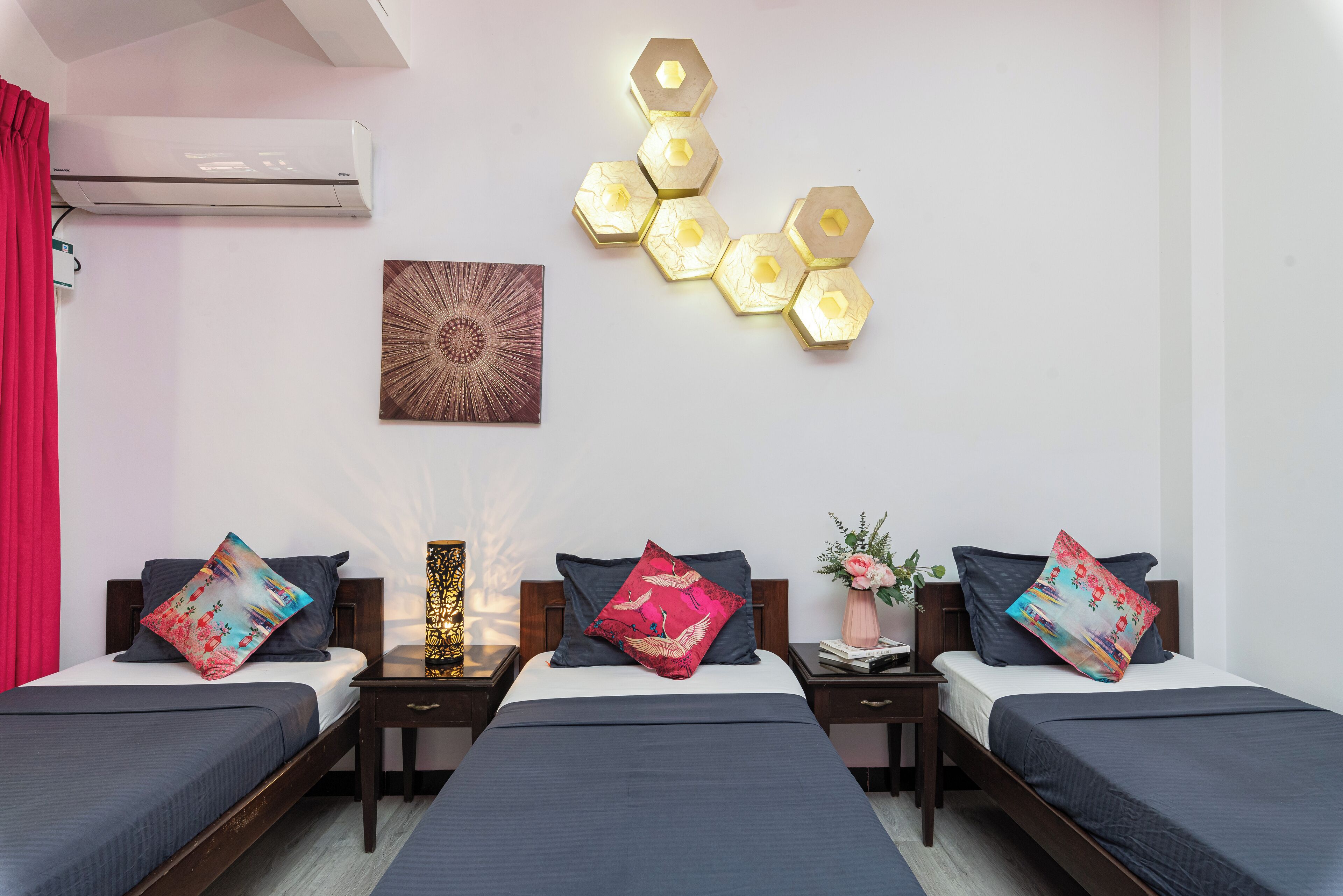 Habitació d'hotel amb un disseny modern, amb un llit central acompanyat per dos llits més petits, una làmpada de paret decorativa i un aire condicionat fixat a la paret.
