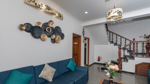 A modern living room with a blue sofa, decorative wall art, a staircase, and a chandelier.
