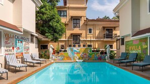 A swimming pool with lounge chairs, surrounded by a building with colorful murals and signs advertising 'Villa Calangute'.