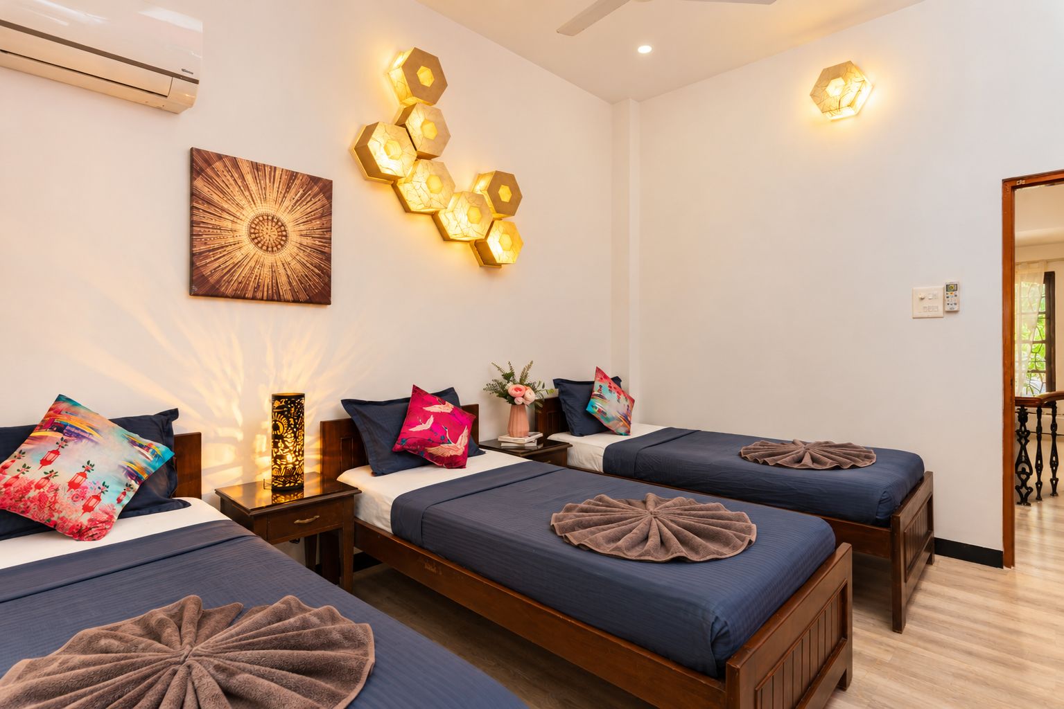A hotel room with two beds, a wall-mounted air conditioner, decorative wall lights, and a large window.