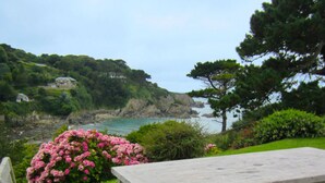 A wooden table and chairs in a garden with a view of the sea and cliffs. - Detached Cottage Overlooking The Sea (Lee)