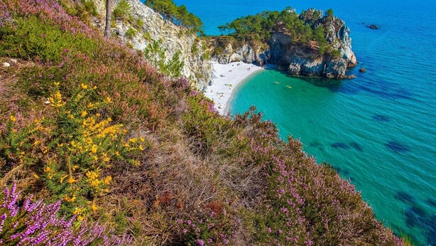 Un paisaje costero con una playa, acantilados rocosos y mar azul transparente.