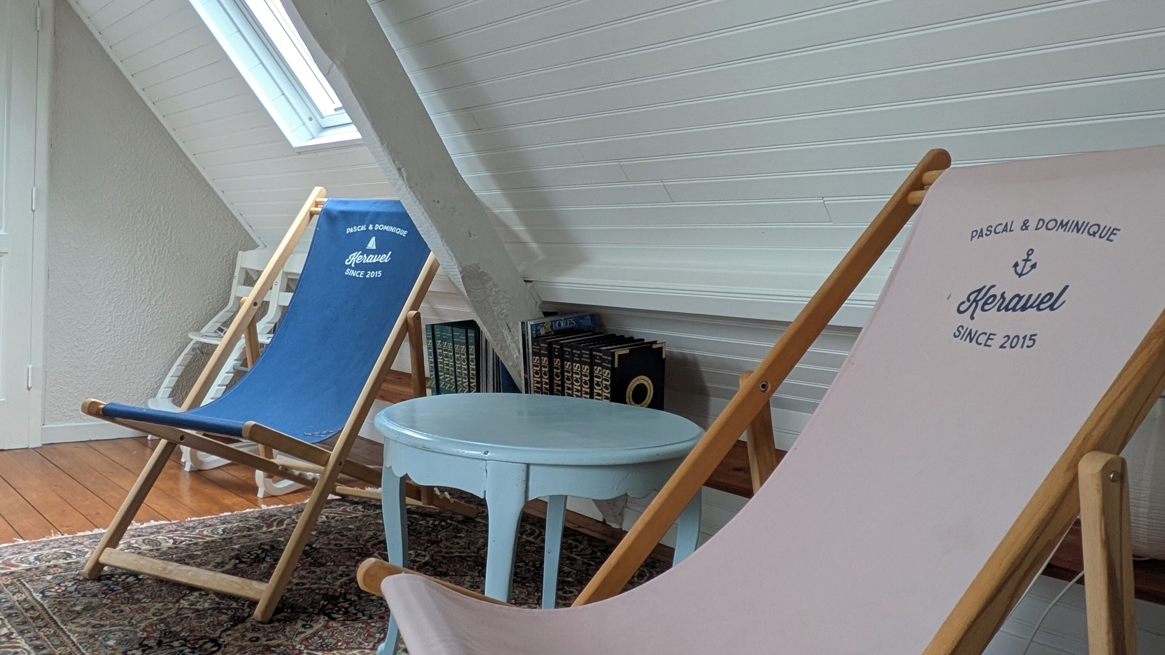 A room with two beach chairs, a small round table, and a bookshelf with books.