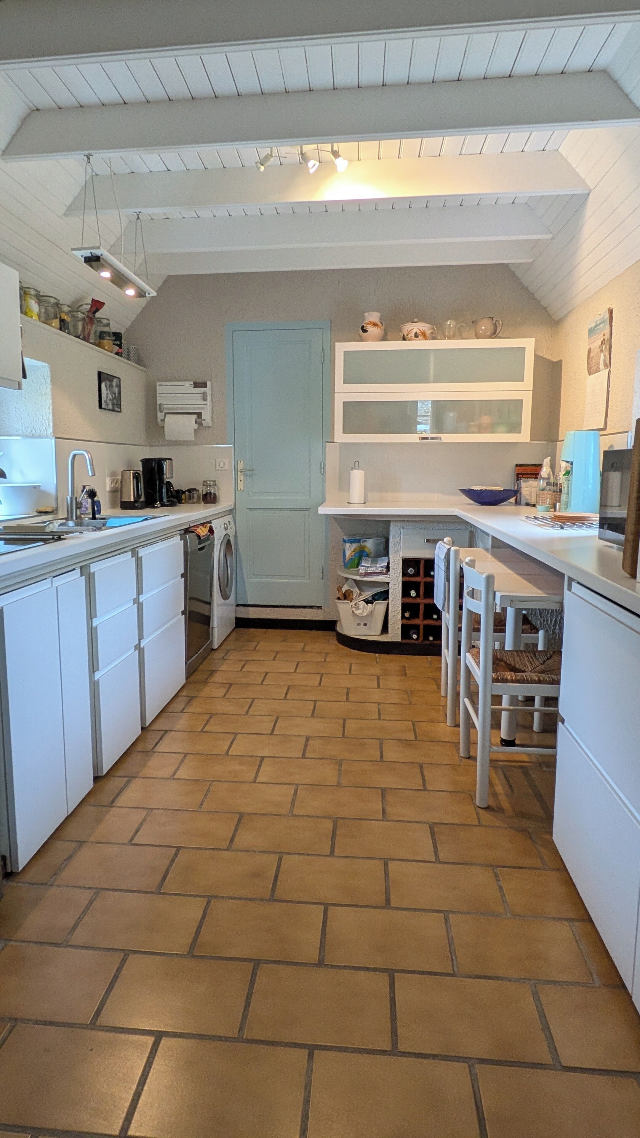 A kitchen with white cabinets, a washing machine, a sink, and a tiled floor.