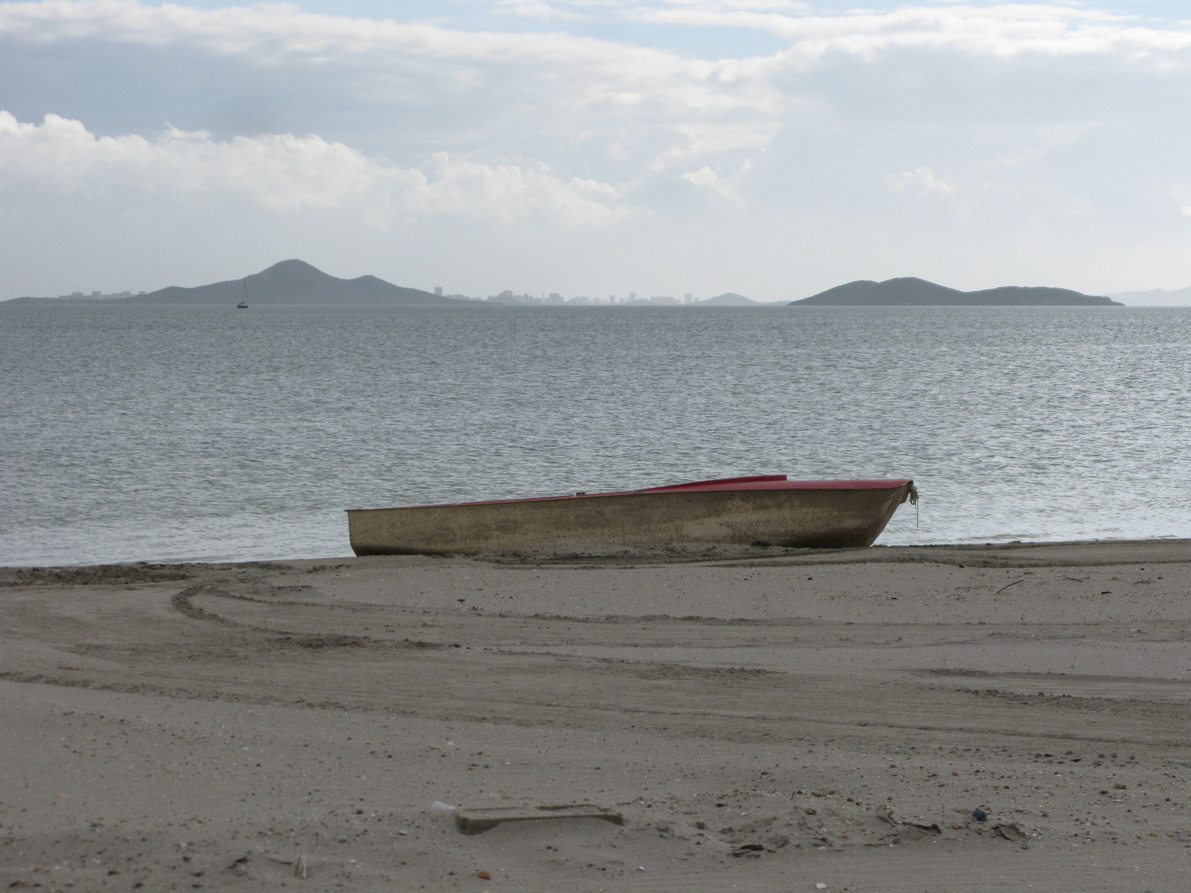 A boat on a sandy beach with calm water and distant mountains.