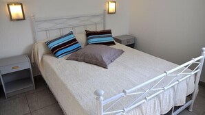 A neatly made bed with a white metal frame, two bedside tables with lamps, and a plain wall. - Alizé T3 for 6 people (San-Nicolao)