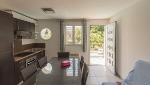 A modern kitchen with dark cabinetry, a round window, and a dining area with a glass table and wicker chairs. - Alizé T3 for 6 people (San-Nicolao)
