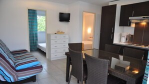 A compact living space with a sofa, dining table, chairs, a TV, a kitchenette, and a small bathroom. - Alizé T3 for 6 people (San-Nicolao)