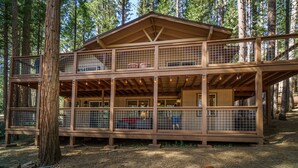 A two-story wooden cabin with a balcony, surrounded by trees.
