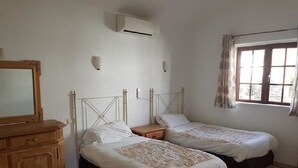 A room with two beds, a wooden dresser, a window with curtains, and an air conditioning unit. - Villa 83 on the complex of Las Brisas  (Playa Blanca)