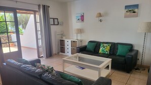 A living room with a black leather sofa, a glass coffee table, a white cabinet, and a black leather couch with green cushions. - Villa 83 on the complex of Las Brisas  (Playa Blanca)