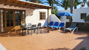 A sunny outdoor patio with a table and chairs, a blue umbrella, and lounge chairs. - Villa 83 on the complex of Las Brisas  (Playa Blanca)