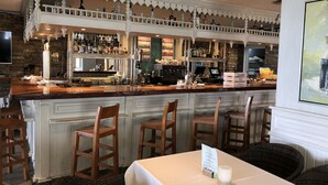 A bar area with a wooden counter, multiple bar stools, and a variety of bottles and glasses.