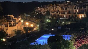 A nighttime view of a hillside residential area with multiple buildings, a swimming pool, and street lighting.