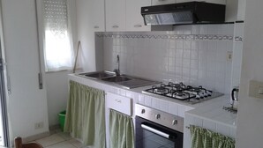 Een keuken met witte kastjes, een gasfornuis, een spoelbak en een groene prullenbak.