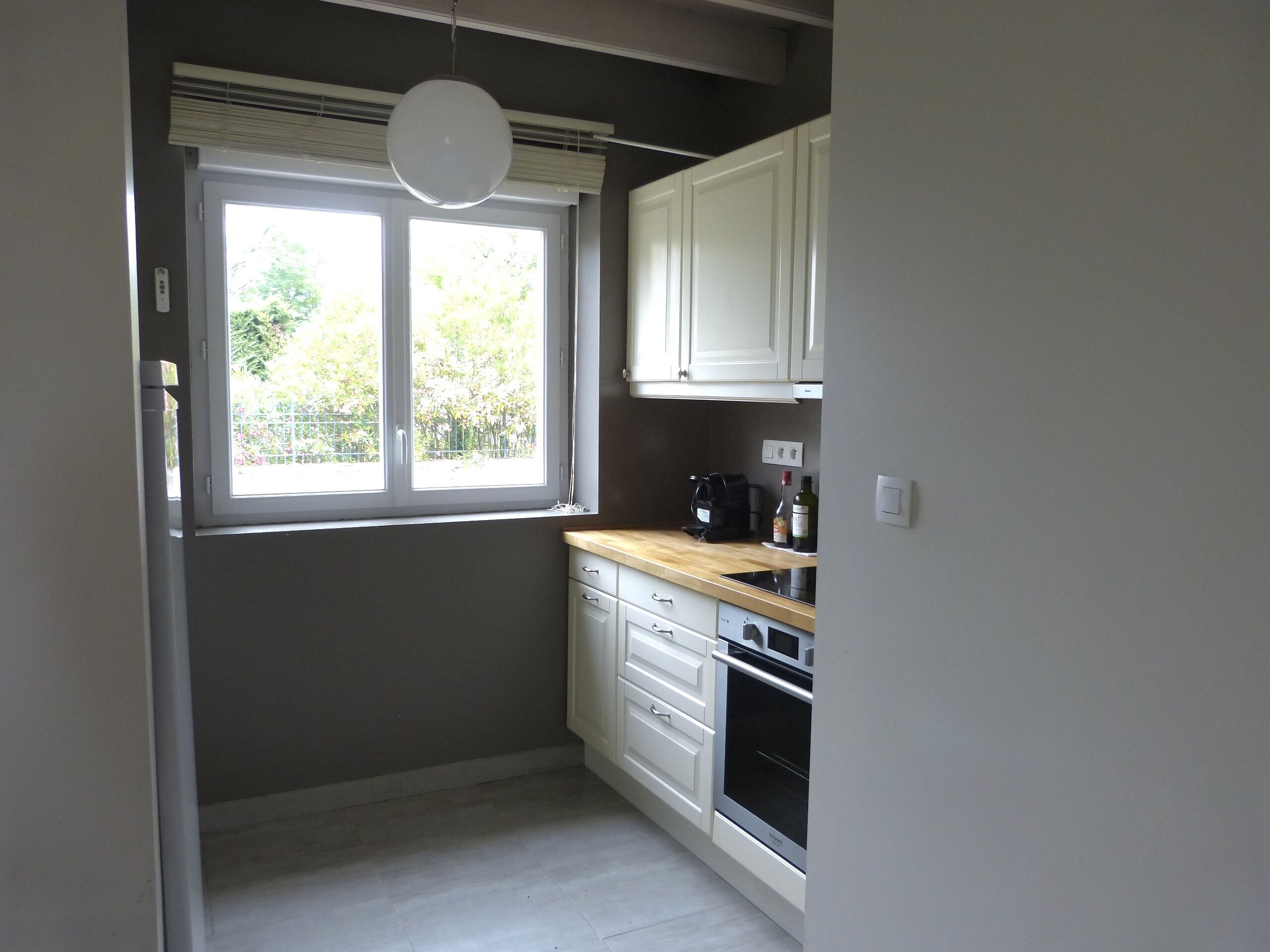 A compact kitchen with white cabinets, a built-in oven, and a window with a view of greenery outside.