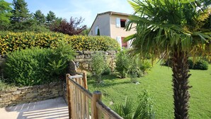 Un jardín con un muro de piedra, valla de madera y una palmera.