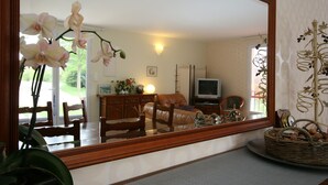 Una sala de estar con un espejo grande que refleja la habitación, un televisor, una mesa de comedor con sillas y una planta decorativa.