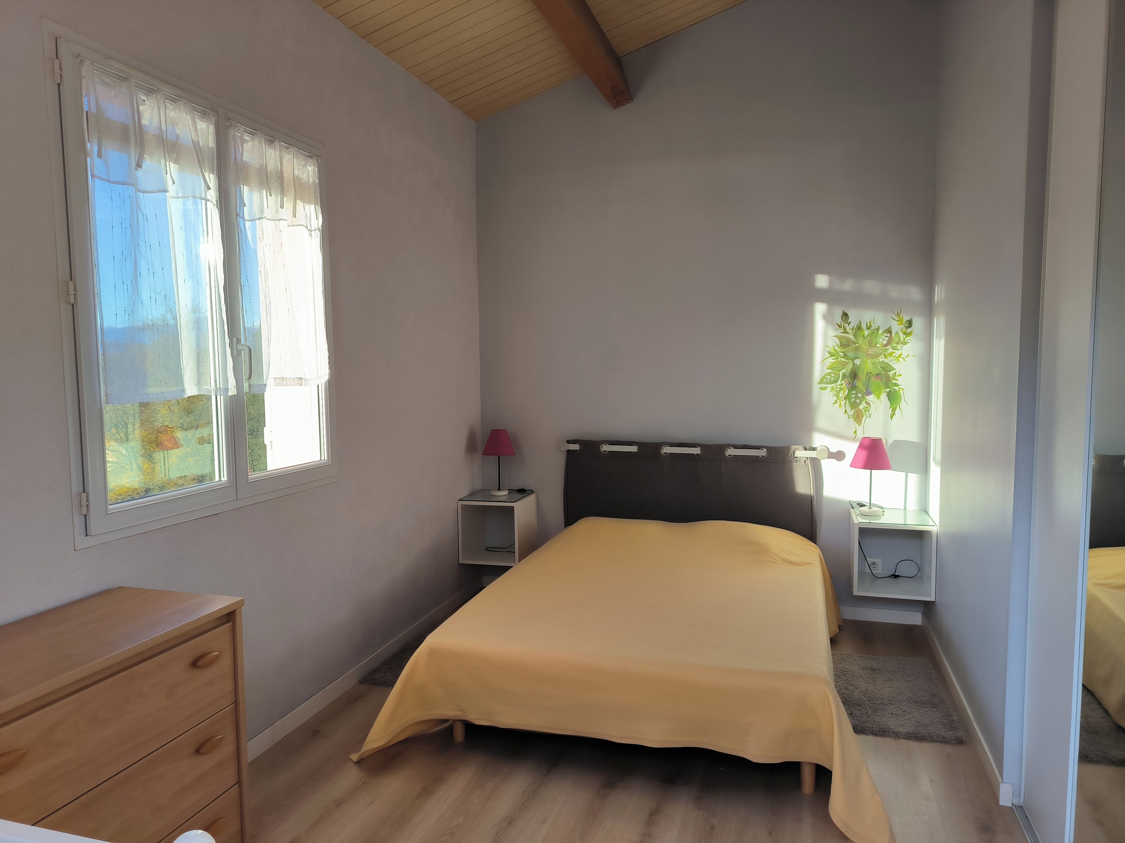 A bedroom with a bed, a nightstand, a dresser, and a window with curtains.