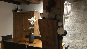 Une table à manger en bois, entourée de chaises, un vase de fleurs blanches et un mur de pierre en arrière-plan.