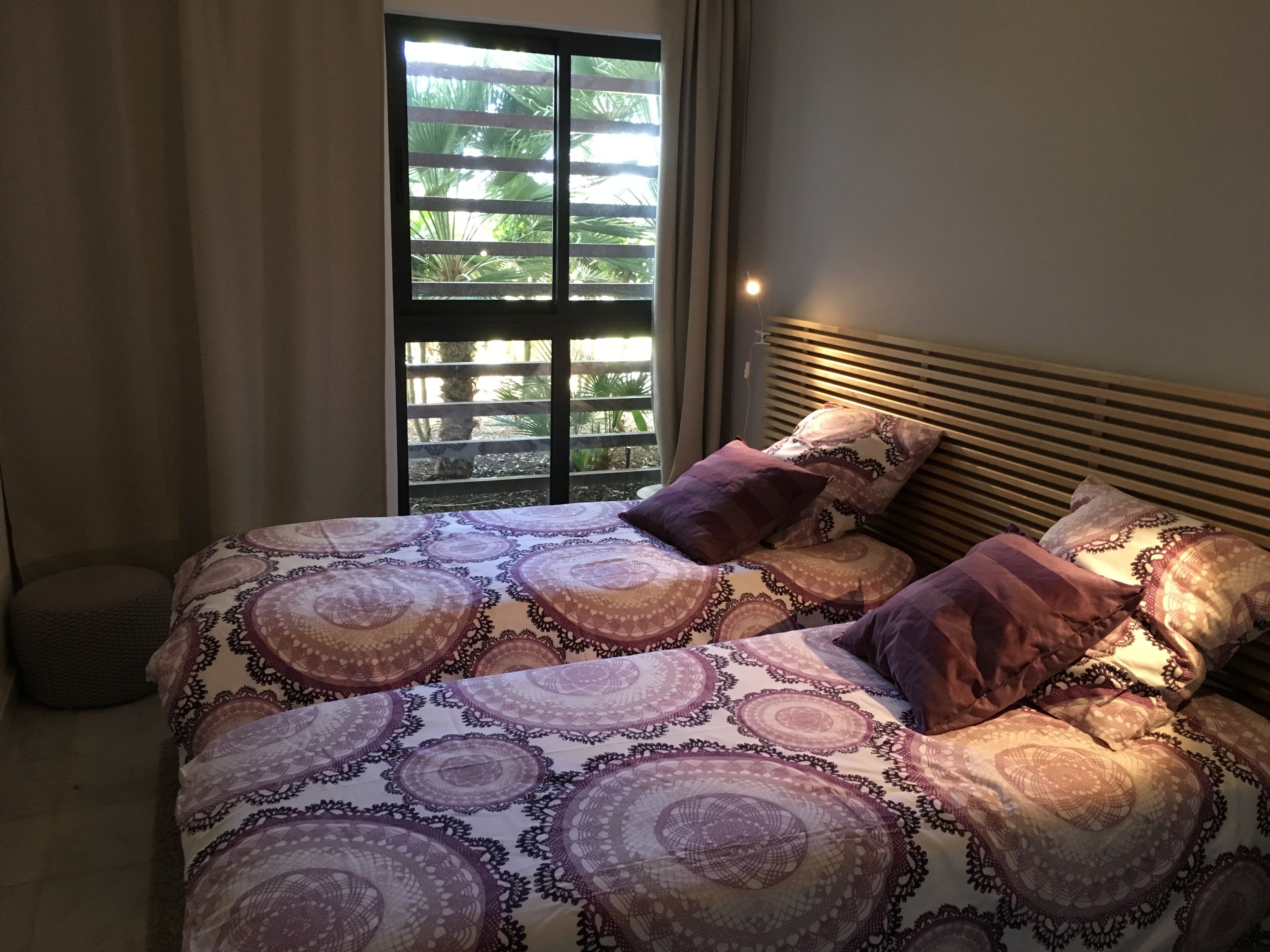 Un lit avec une couvre-lit à motifs et plusieurs oreillers, une fenêtre avec des stores et une lampe de chevet.