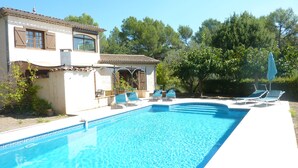 Ett område vid poolen med en pool, solstolar och en byggnad med fönster och fönsterluckor.