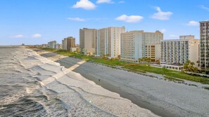 Um hotel à beira-mar com vários edifícios altos, uma praia de areia e um píer ao fundo.