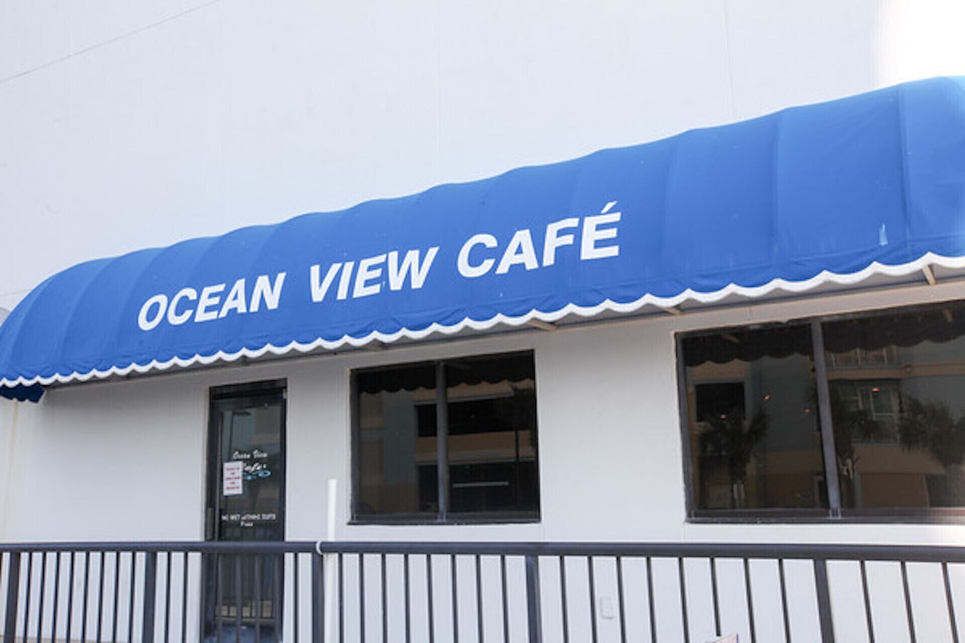 Una cafetería con toldo azul y pared exterior blanca.