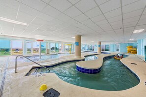 Piscina interior com placa indicando profundidade de 3 pés, posto de salva-vidas e vista para o exterior.
